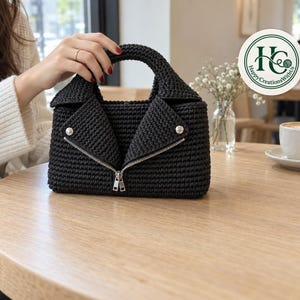 May include: A black crocheted handbag shaped like a motorcycle jacket, featuring a structured collar, a silver-toned metal zipper closure, and a circular handle. A circular logo in the corner displays the text Happy CreationsWithUs.
