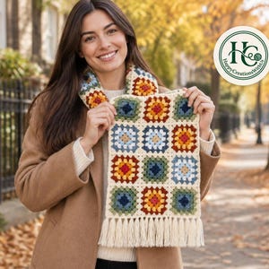 Könnte beinhalten: Ein handgefertigter Häkelschal mit einem Muster aus bunten Granny Squares in Rot-, Gelb-, Blau- und Grüntönen, die mit cremefarbenem Garn verbunden sind. Der Schal hat am unteren Rand eine lange cremefarbene Fransenborte.