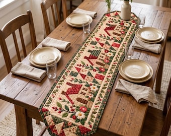 May include: A rectangular quilted table runner featuring a repeating pattern of small houses, red and green geometric quilt blocks, and floral motifs with white daisies and red berries on a cream background with a dark green border.