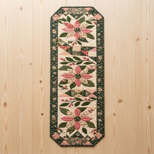 Modern Patchwork Bloom quilted table runner PDF pattern with dusty pink floral blocks, sage green leaves, cream fabric, geometric patchwork accents, and dark green floral borders. Three large flower motifs and leafy branches create an elegant botanical design for dining tables. Finished size 16 x 54 inches (40.6 x 137.2 cm).