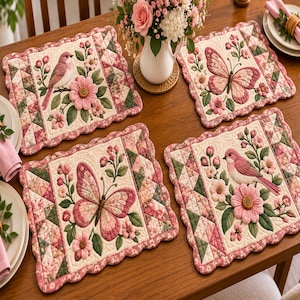 May include: A set of four rectangular quilted placemats featuring scalloped edges, pink butterflies, pink birds, and floral motifs in shades of pink and green on a cream background, arranged on a wooden table with a white flower vase.