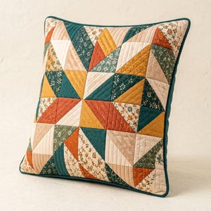 May include: A square quilted throw pillow featuring a geometric star pattern composed of triangular fabric patches. The design incorporates a color palette of mustard yellow, burnt orange, deep teal, and cream, with floral and solid textures.