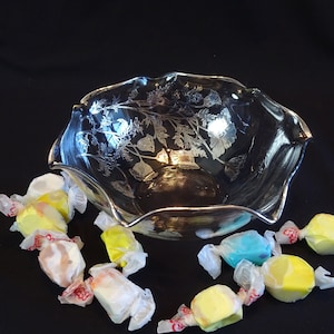 May include: A clear glass bowl with a scalloped edge and a floral design etched into the glass. The bowl is filled with colorful candies wrapped in white paper.