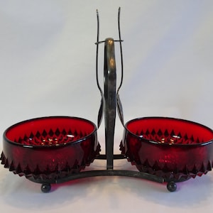 May include: A set of two ruby red glass bowls with a diamond pattern on a silver metal stand. The stand has a handle on top.