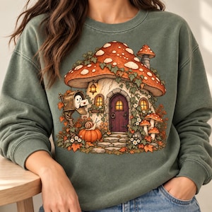 Könnte beinhalten: Ein salbeigrünes Sweatshirt mit Rundhalsausschnitt und einem Grafikdruck eines pilzförmigen Hauses mit großem rot gepunktetem Hut, einer violetten Tür, einem Briefkasten mit einem Geist, der einen Brief hält, einem Kürbis und einer Schnecke.
