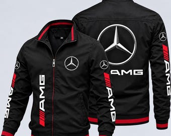 Puede incluir: Una chaqueta negra con cremallera y detalles rojos en el cuello, los puños y el dobladillo. El frente y la espalda muestran el logotipo de Mercedes-Benz y el texto AMG en blanco. Las mangas incluyen logotipos AMG y rayas rojas.