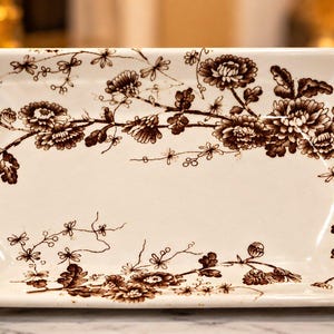May include: A rectangular ceramic serving tray with a cream-colored base and a dark brown floral transferware pattern. The tray features scalloped edges, integrated side handles, and a detailed botanical design of blooming flowers.