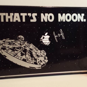 May include: A black laptop with a Star Wars themed design featuring the Millennium Falcon and the text "THAT'S NO MOON."  A dark grey bust of Darth Vader is in the background.