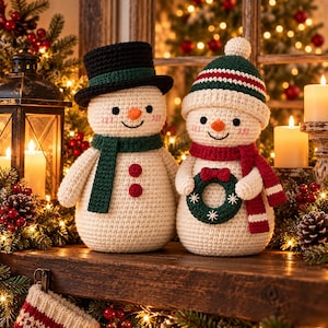 May include: Two crocheted snowman figures made of cream-colored yarn. The left snowman wears a black top hat with a green band and a green scarf. The right snowman wears a green, white, and red striped hat and a red scarf, holding a small green wreath.