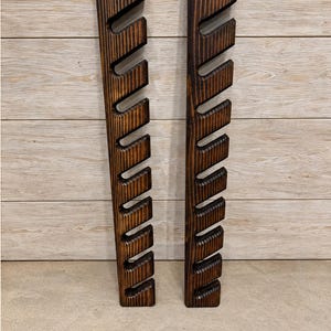 May include: Two vertical dark brown stained wooden wall racks featuring a series of angled, evenly spaced notches cut into the side of each piece. The wood grain is visible throughout the surface of both long, narrow, rectangular storage units.