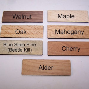 May include: A collection of rectangular wooden samples, each labeled with a different wood type: Walnut, Maple, Oak, Mahogany, Blue Stain Pine, Cherry, and Alder. The wood grains vary in color and texture.