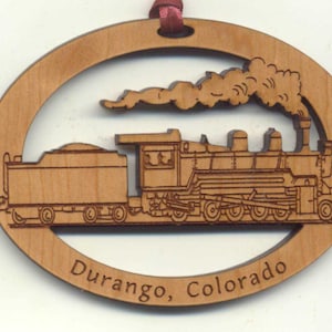 May include: Wooden oval ornament with a laser-cut design of a steam train with smoke billowing from the chimney. The ornament is inscribed with "Durango, Colorado".