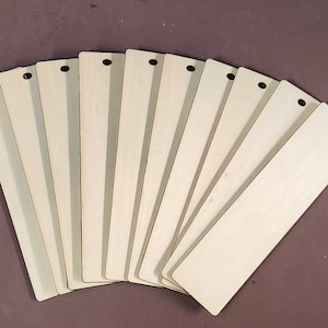 May include: Ten blank wooden bookmarks with rounded edges and a hole punched at the top. The bookmarks are arranged in a fan shape.