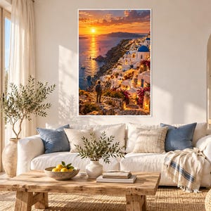 Op de afbeelding: Een rechthoekige wandkunstprint met een zonsondergang over een kustdorp met witte gebouwen, blauwe koepels en felroze bloemen. Een persoon staat op een stenen pad met uitzicht op de zee en de laagstaande zon.