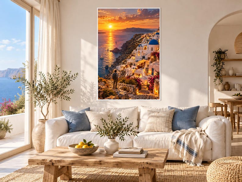 Op de afbeelding: Een rechthoekige wandkunstprint met een zonsondergang over een kustdorp met witte gebouwen, blauwe koepels en felroze bloemen. Een persoon staat op een stenen pad met uitzicht op de zee en de laagstaande zon.