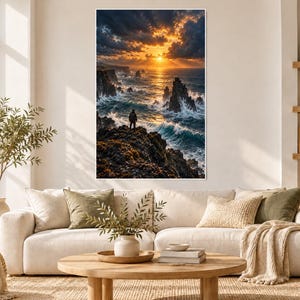 Op de afbeelding: Een ingelijste wandkunstprint met een eenzame figuur die op een donkere, grillige klif staat en uitkijkt over een turbulente oceaan bij zonsondergang. De lucht is gevuld met dramatische, goudkleurige wolken en golven.