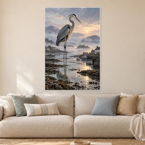 Op de afbeelding: Een verticale wandkunstprint met een grote grijze reiger die bij zonsopgang in ondiep kustwater staat. De sc&egrave;ne bevat een mistige kustlijn, kleine boten en verre heuvels onder een zachte lucht met wolken.