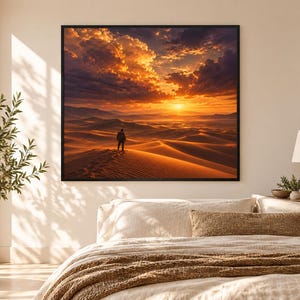 Pode incluir: Uma impress&atilde;o de arte de parede quadrada apresentando uma paisagem des&eacute;rtica ao p&ocirc;r do sol com uma figura solit&aacute;ria em uma duna sob um c&eacute;u laranja e roxo. A obra &eacute; emoldurada com uma borda preta fina em uma parede branca.