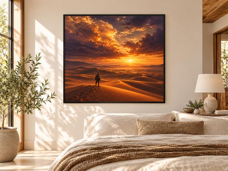 Pode incluir: Uma impress&atilde;o de arte de parede quadrada apresentando uma paisagem des&eacute;rtica ao p&ocirc;r do sol com uma figura solit&aacute;ria em uma duna sob um c&eacute;u laranja e roxo. A obra &eacute; emoldurada com uma borda preta fina em uma parede branca.