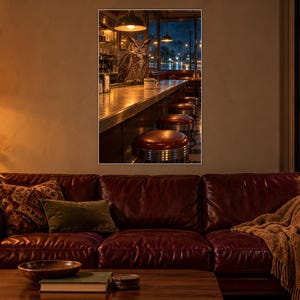 May include: A framed wall art print depicting a diner interior at night with a great horned owl perched on the counter. The scene features a long bar, red vinyl stools, and warm overhead lighting, creating a moody atmosphere in a dark room.