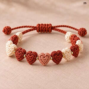 Puede incluir: Una pulsera con corazones de ganchillo alternados en tonos óxido, crema y rosa claro, separados por pequeñas cuentas doradas. La pulsera tiene un cordón color óxido con un cierre de nudo deslizante y dos extremos anudados.