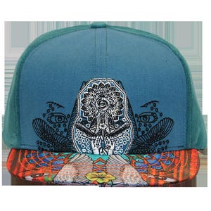 May include: A teal blue and black patterned baseball cap with a colorful, patterned brim. The cap features a black and white embroidered design of a stylized face with a third eye.