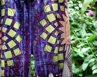 May include: Close-up of patterned pants with a drawstring. The fabric features a vibrant design with purple, blue, and peach tones. Geometric shapes and bird-like illustrations are visible on the material. The pants are in a casual style.