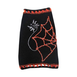May include: Black knitted dog sweater with an orange and white crocheted trim. The sweater features a white spider web design with an orange spider.