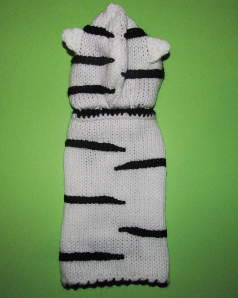 Peut inclure: Pull-over en tricot blanc pour chien avec des rayures noires et une capuche. La capuche a deux petites oreilles.