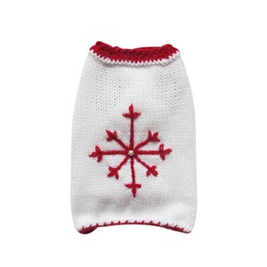 May include: White knitted dog sweater with a red snowflake design and a pearl button in the center.