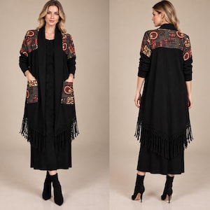 May include: A long black open-front cardigan featuring a patterned yoke and matching patch pockets in shades of red, orange, and gold. The garment has long sleeves and a pointed hemline finished with long black fringe trim.