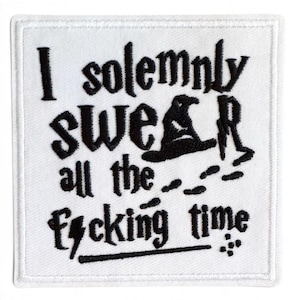 May include: A square white fabric patch featuring black embroidered text which reads I solemnly swear all the f*cking time. The design incorporates a small black embroidered witch hat and a lightning bolt symbol within the lettering.