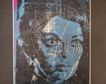 May include: A rectangular print featuring a high-contrast, stylized portrait of a person in shades of blue, black, and white. A spiderweb pattern is overlaid across the face, with a thin vertical strip of bright magenta on the left edge.