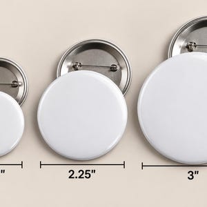 May include: Three circular white pin-back buttons with metallic silver backs and pin fasteners. The buttons are arranged in increasing size, with labels indicating diameters of 1.25 inches, 2.25 inches, and 3 inches respectively.