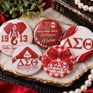 May include: Five circular pinback buttons featuring Delta Sigma Theta sorority branding. Designs include an elephant, the Greek letters ΔΣΘ, the text Intelligence is the Torch of Wisdom, hands forming a triangle, and a red gingham bow pattern.
