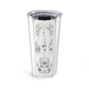 Puede incluir: Un vaso de viaje blanco con tapa transparente que presenta un diseño gráfico vertical de fases lunares, cristales, una polilla, un ojo y una mano sosteniendo una varita. El texto Witchy Vibes está impreso en la parte inferior del diseño.