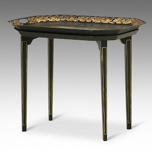 May include: A black rectangular tray table with four straight legs. The tray top features a gold floral pattern along the rim. The legs and the frame of the table are decorated with thin vertical gold lines. The surface is smooth and dark.
