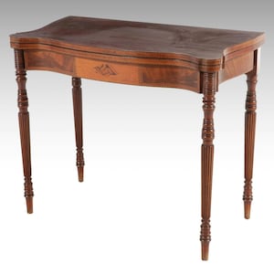 May include: A brown wooden console table with a rectangular top featuring curved edges. The table has four slender, fluted legs and a central front panel with a decorative inlay. The wood grain is visible across the surface and frame.