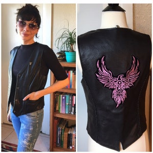 May include: Black leather vest with a pink phoenix design on the back. The vest has a zipper closure and two pockets.