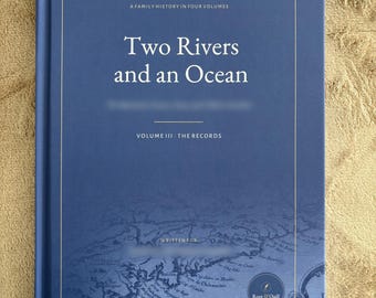 Peut inclure: Un livre relié bleu intitulé Two Rivers and an Ocean, A Family History in Four Volumes, Volume III - The Records. La couverture présente une fine bordure dorée et une illustration de carte historique détaillée avec un logo circulaire Root & Quill.
