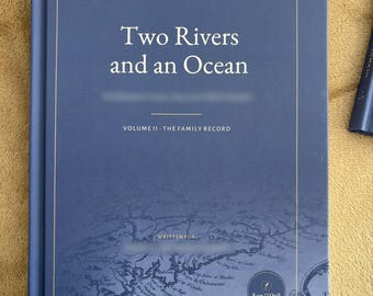 May include: A blue hardcover book titled Two Rivers and an Ocean, A Family History in Four Volumes, Volume II - The Family Record. The cover features a gold-lined border and a faint, detailed historical map illustration with a circular logo.