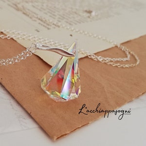 Pode incluir: Colar de corrente prateada com um pendente em forma de prisma iridescente. O pendente exibe um espectro de cores. O colar repousa sobre um pedaço de papel castanho com o texto "L'acchiappasogni" em itálico.