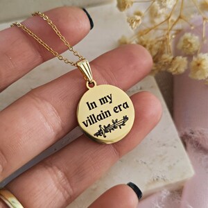 May include: Gold necklace with a round pendant that says "In my villain era" with a small sword design.