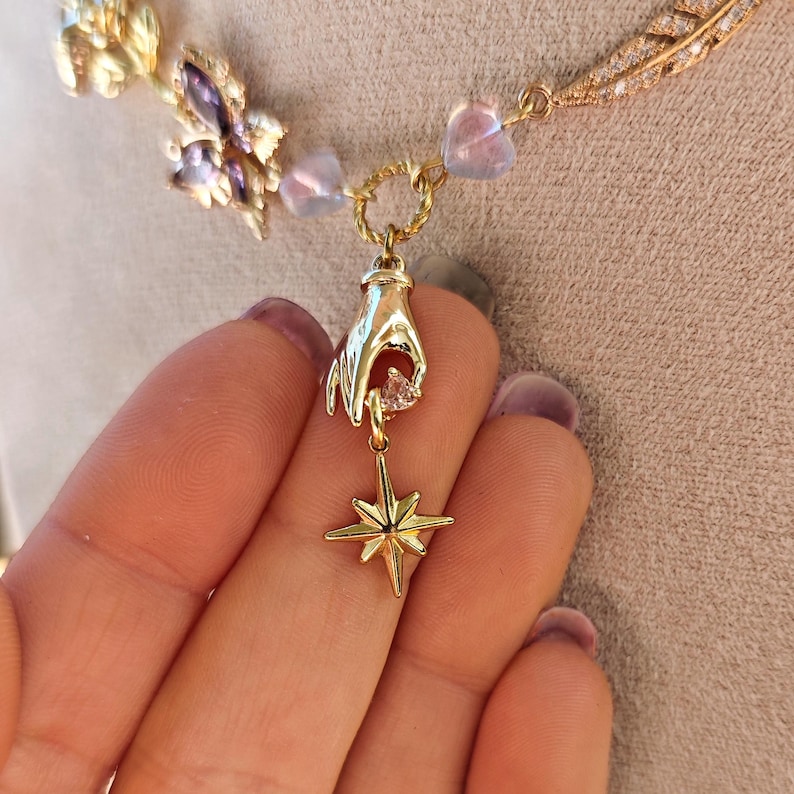 May include: Gold necklace with a hand holding a small crystal and a star pendant.