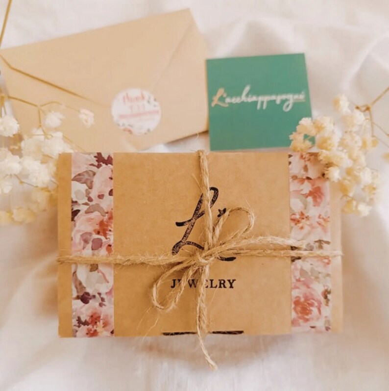 May include: A brown cardboard box with a floral design and a brown twine bow. The box is labeled "LJ Jewelry".
