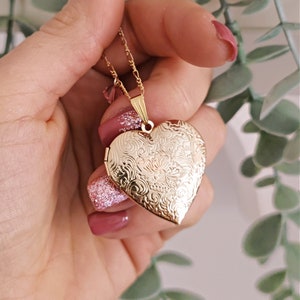 May include: A gold heart-shaped locket necklace with an intricate floral design. The locket is open and the chain is visible.
