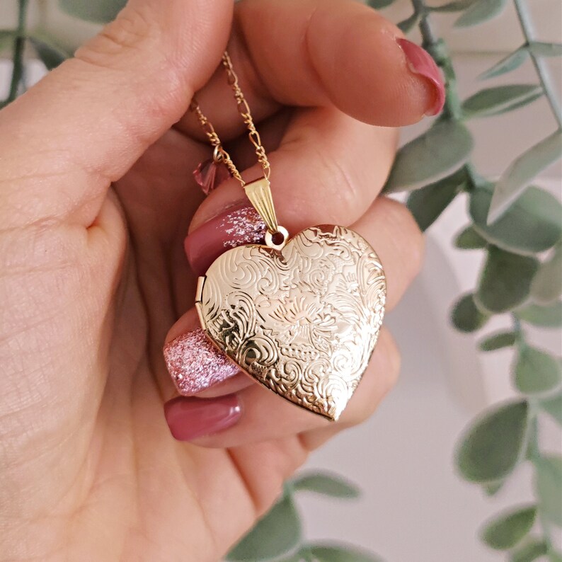 May include: A gold heart-shaped locket necklace with an intricate floral design. The locket is open and the chain is visible.