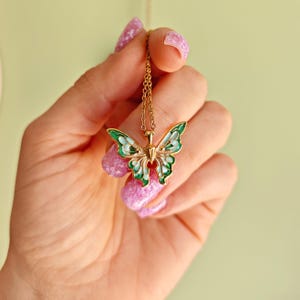 May include: Gold-toned butterfly pendant necklace with green and white enamel detailing. The butterfly design features intricate cutouts and a delicate chain. A charming accessory for everyday wear.