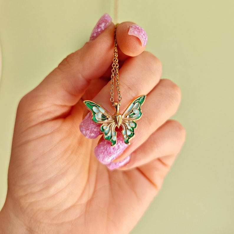 May include: Gold-toned butterfly pendant necklace with green and white enamel detailing. The butterfly design features intricate cutouts and a delicate chain. A charming accessory for everyday wear.