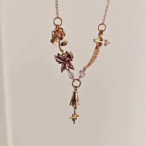 May include: A gold necklace with a variety of charms, including a rose, a butterfly, a hand, and a star. The charms are connected by a chain and beads.